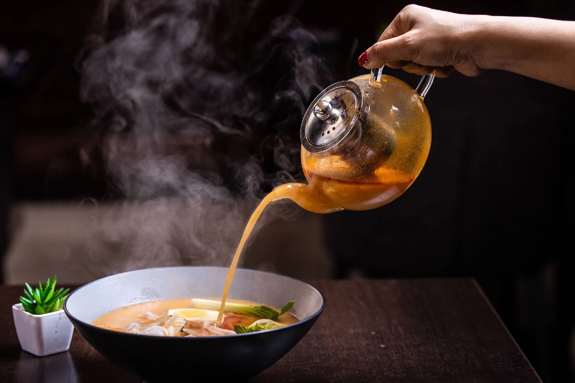 Steam rising from an elegant teapot above a bowl of soup
